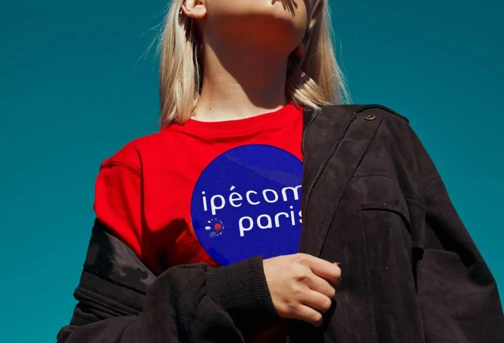 Jeune femme en t-shirt rouge avec le logo Ipécom Paris, regard tourné vers le ciel