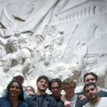 Groupe de Terminale posant devant une sculpture murale imposante au Louvre, dans le cadre de leur parcours philosophique.