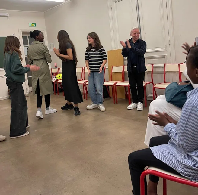 Des élèves de collège reçoivent les applaudissements après une scène de théâtre en anglais.