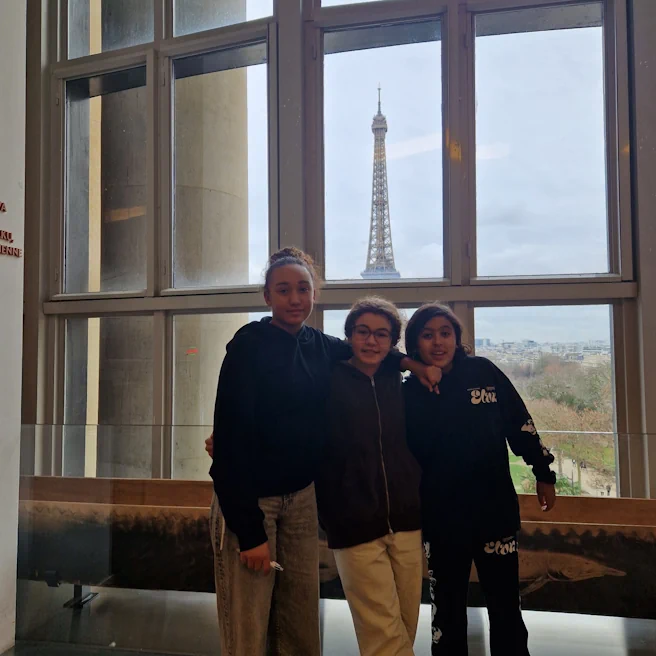 Trois élèves posent devant une fenêtre panoramique du Musée de l’Homme avec la Tour Eiffel en arrière-plan